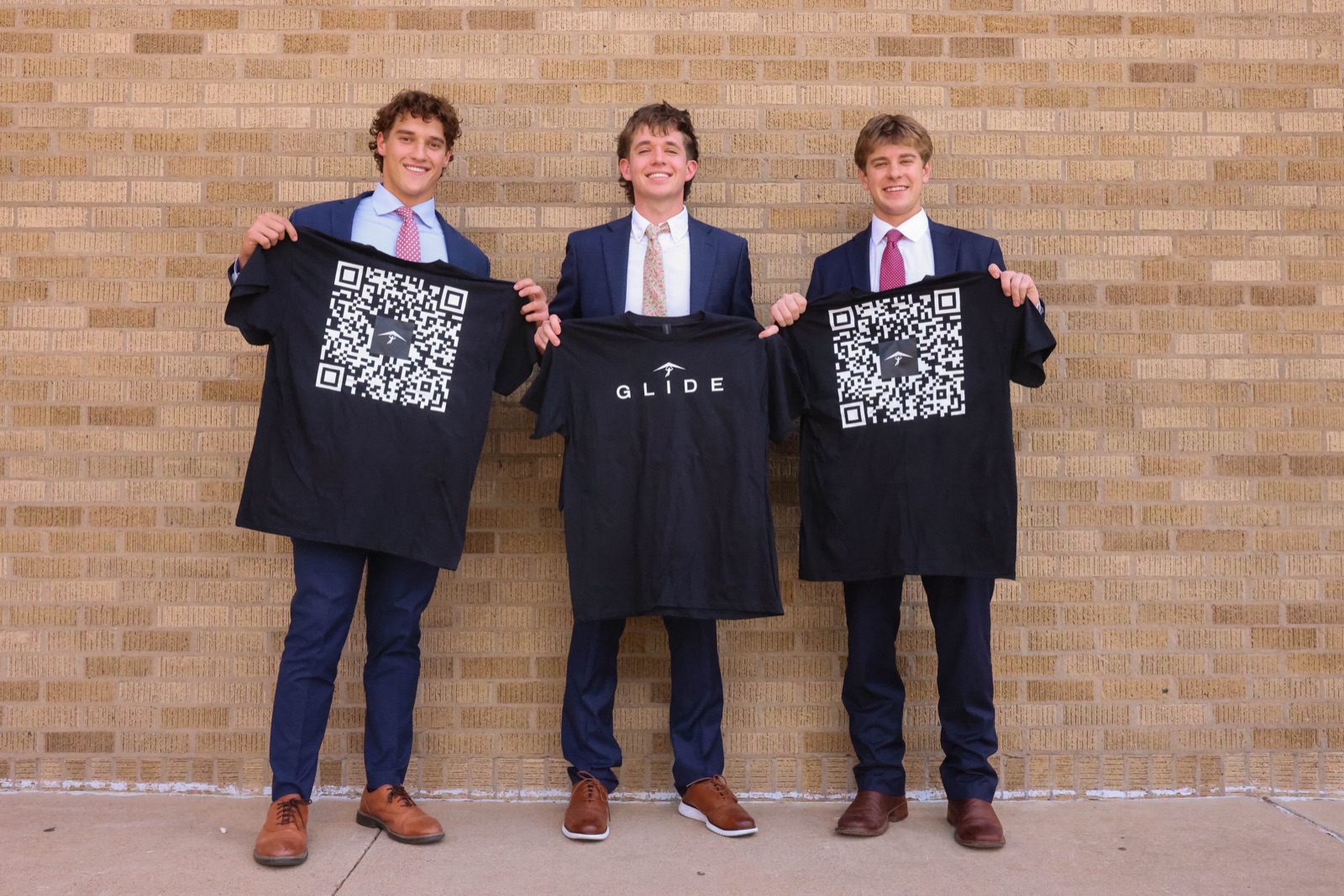 William, Grant and Grayson holding Glide shirts against a brick wall